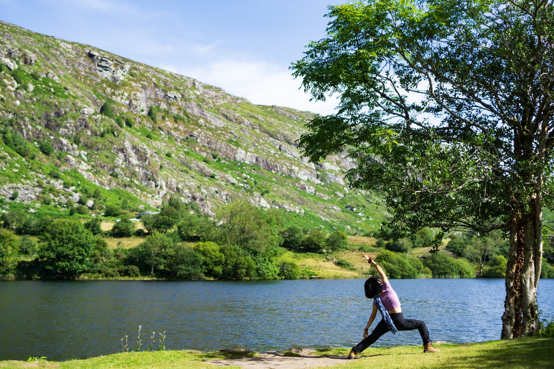 woman in black tank top and black leggings sitting on tree branch near lake during daytime