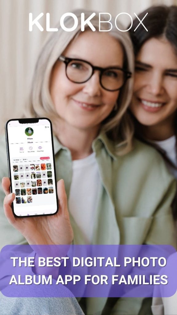 promotional lifestyle image for the Klokbox app features a close-up of an older woman with silver hair and glasses, smiling as she holds up a smartphone displaying the Klokbox app interface. Behind her, a younger woman with long dark hair leans in, smiling warmly. The smartphone screen showcases a family photo album with a circular profile picture labeled "Willow" at the top, and a grid of images below, organized within the app. The background is softly blurred, focusing on the two women and the phone screen. Overlaid in the bottom third of the image is a semi-transparent purple banner with bold white text stating, "THE BEST DIGITAL PHOTO ALBUM APP FOR FAMILIES." The "KLOKBOX" logo appears at the top in white, ensuring brand visibility.